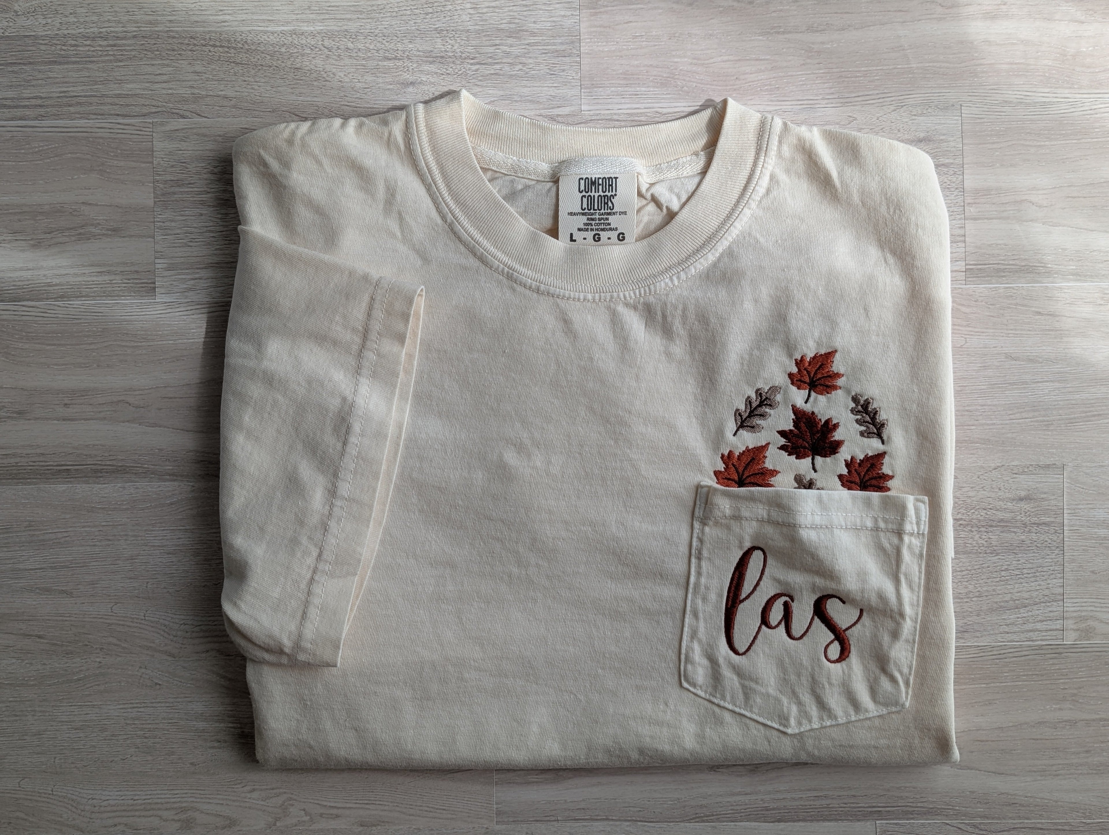 Folded cream Comfort Colors pocket tee with fall leaf and monogram embroidery
