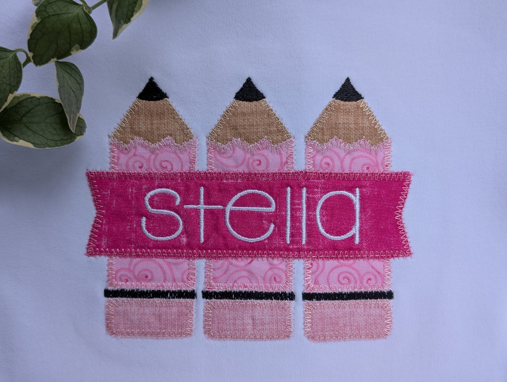 Close up of pink pencil applique with personalized name Stella on white tee