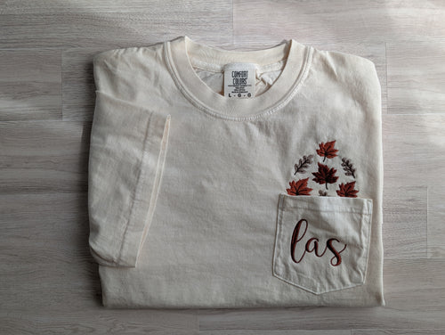 Folded cream Comfort Colors pocket tee with fall leaf and monogram embroidery