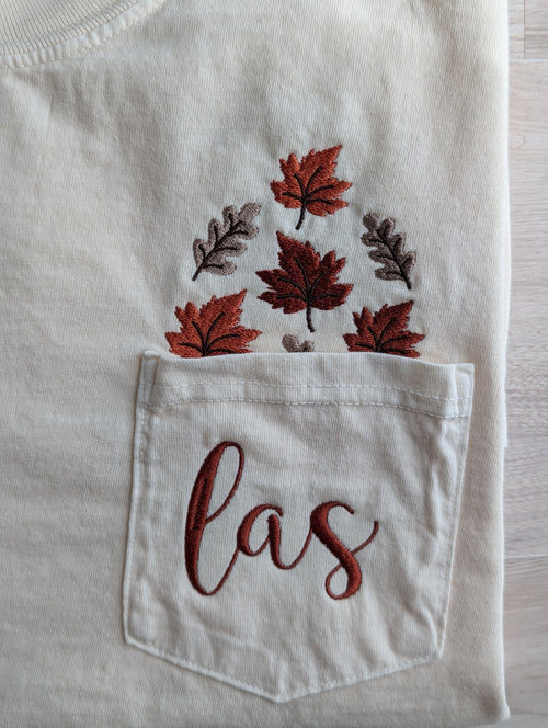 Close up of fall leaf embroidery and custom monogram on cream Comfort Colors pocket tee