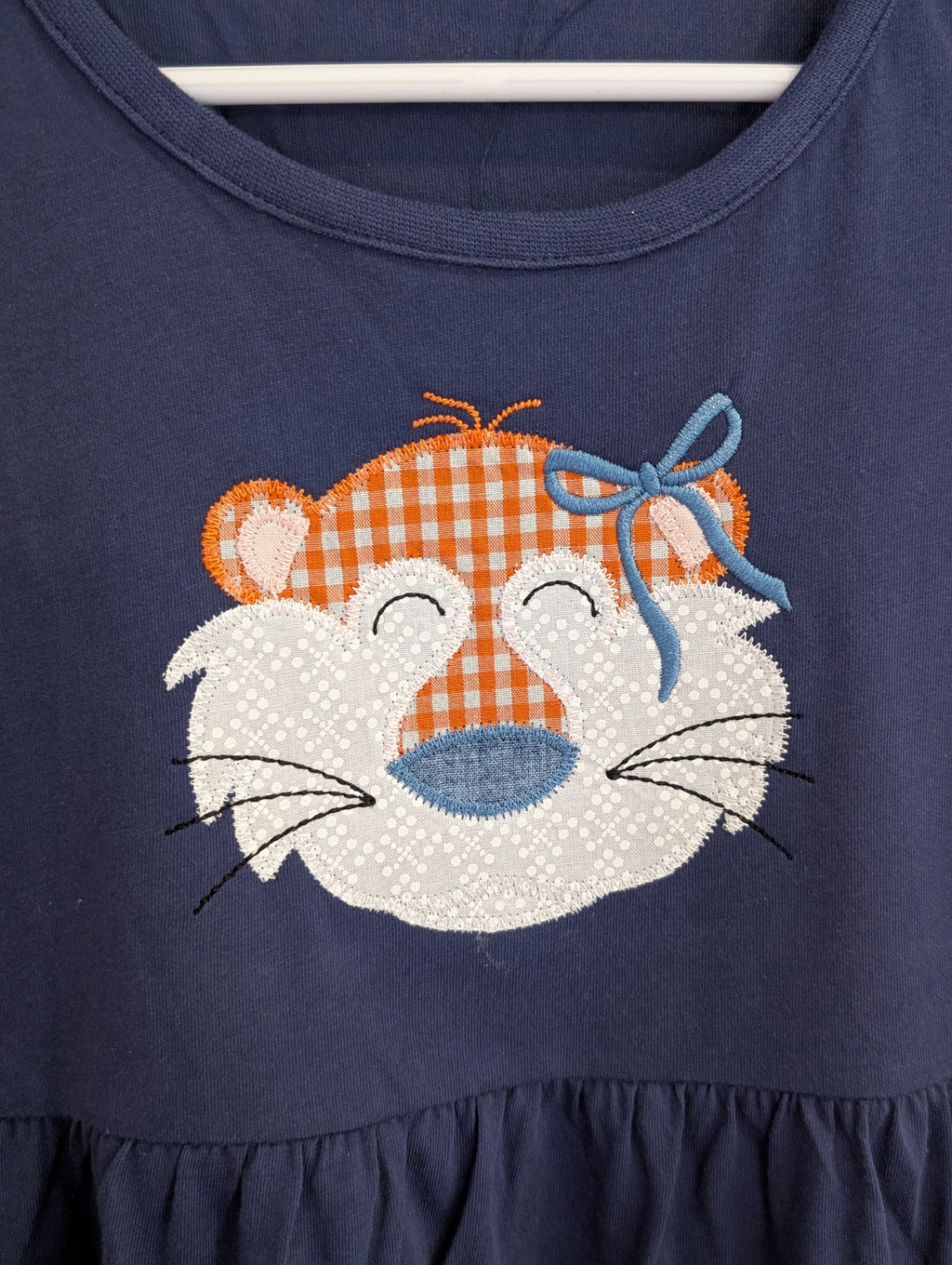 Close-up of tiger face appliqué in orange gingham with blue bow on navy dress