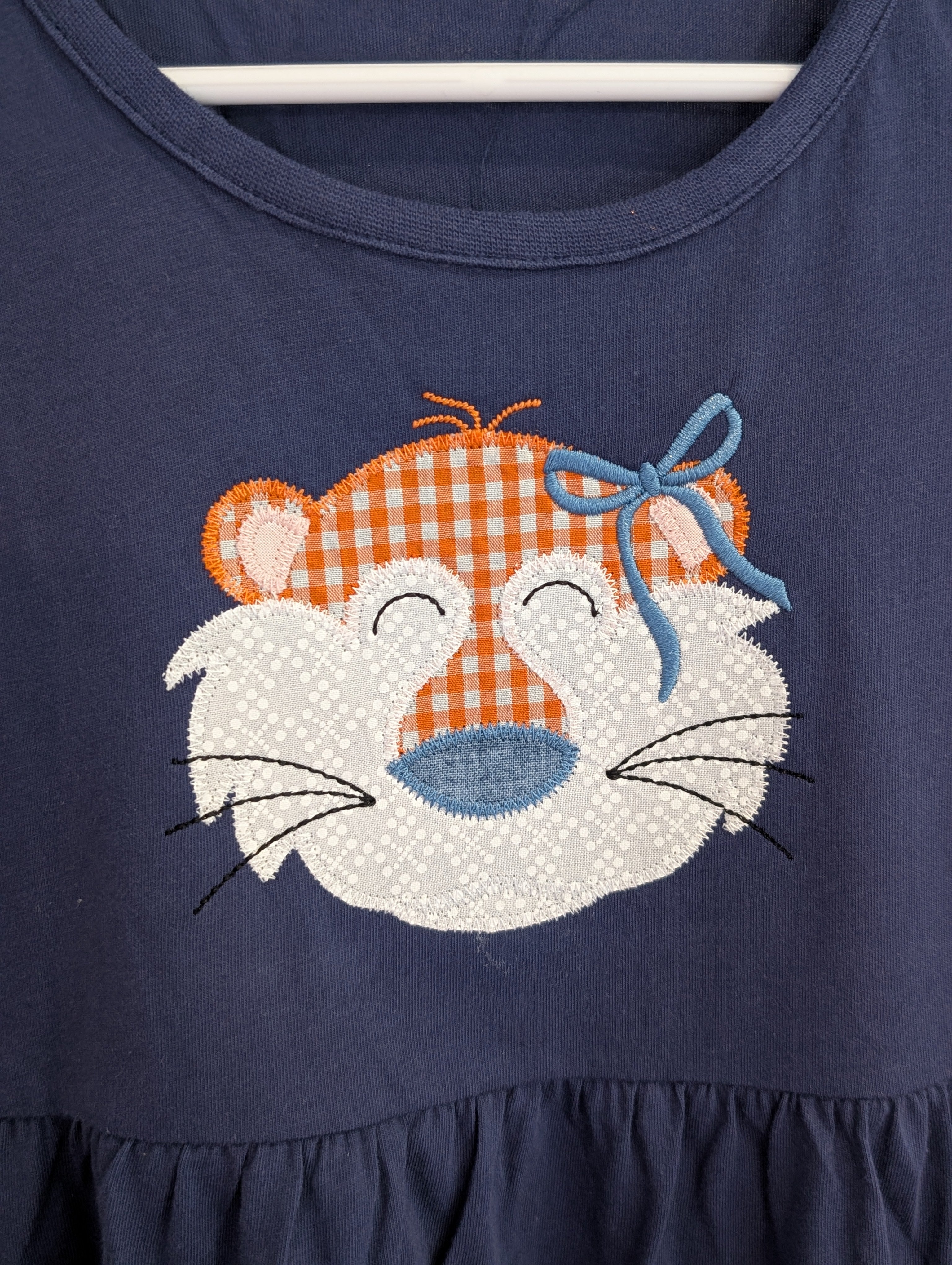 Close-up of tiger face appliqué in orange gingham with blue bow on navy dress