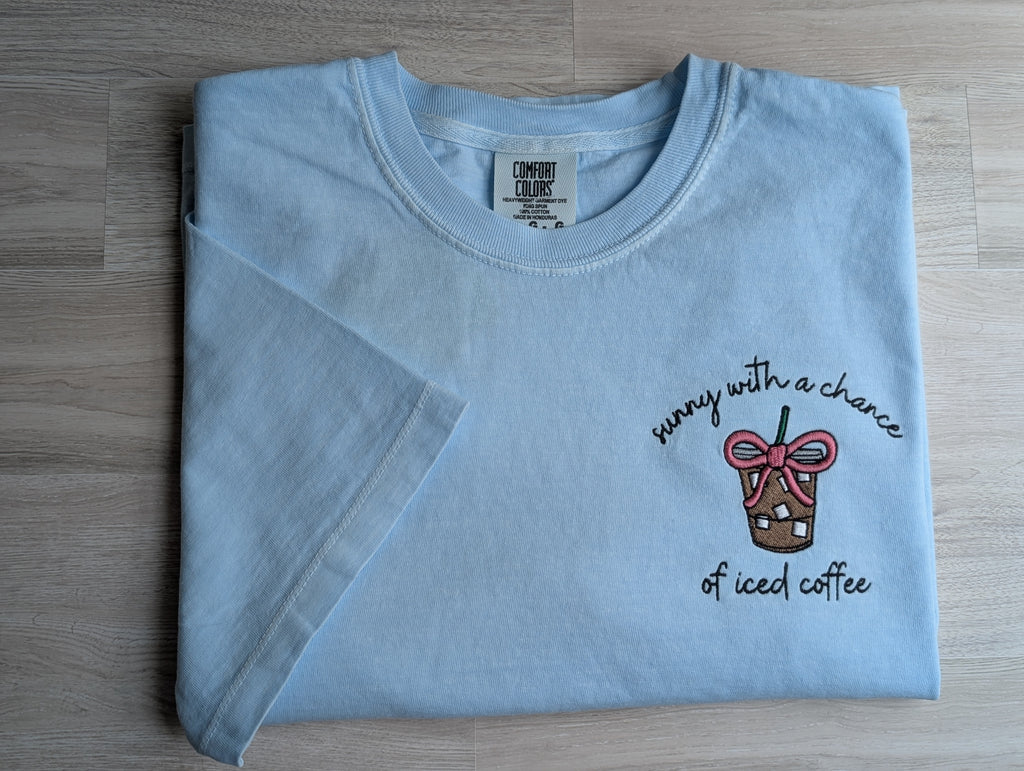 Folded light blue Comfort Colors tee with sunny with a chance of iced coffee embroidered design