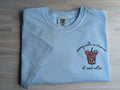 Folded light blue Comfort Colors tee with sunny with a chance of iced coffee embroidered design