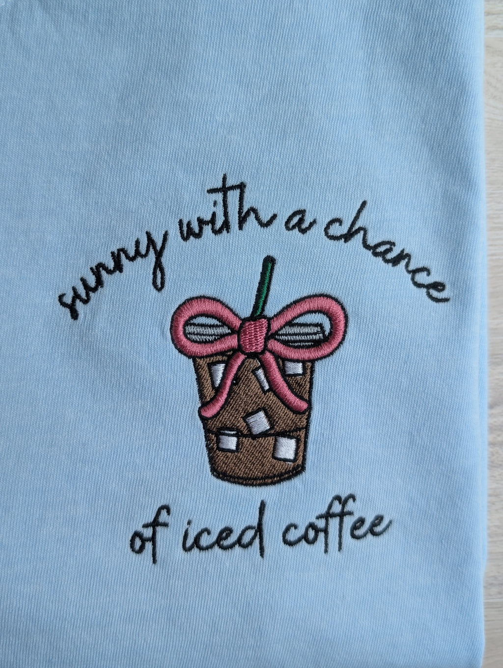 Close-up of iced coffee cup embroidery with pink bow on light blue tee