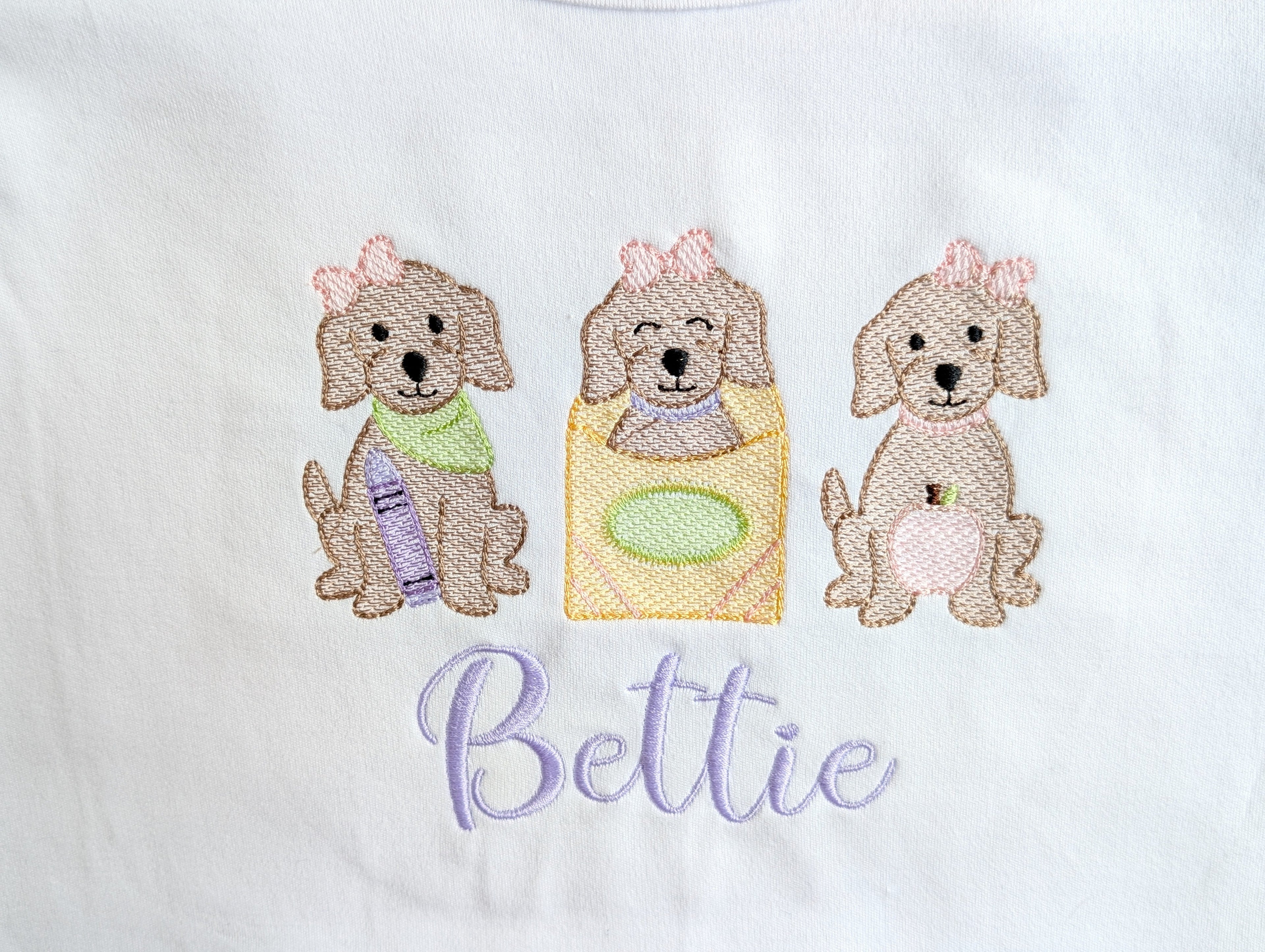 Close-up of puppy trio embroidery detail on onesie with name Bettie