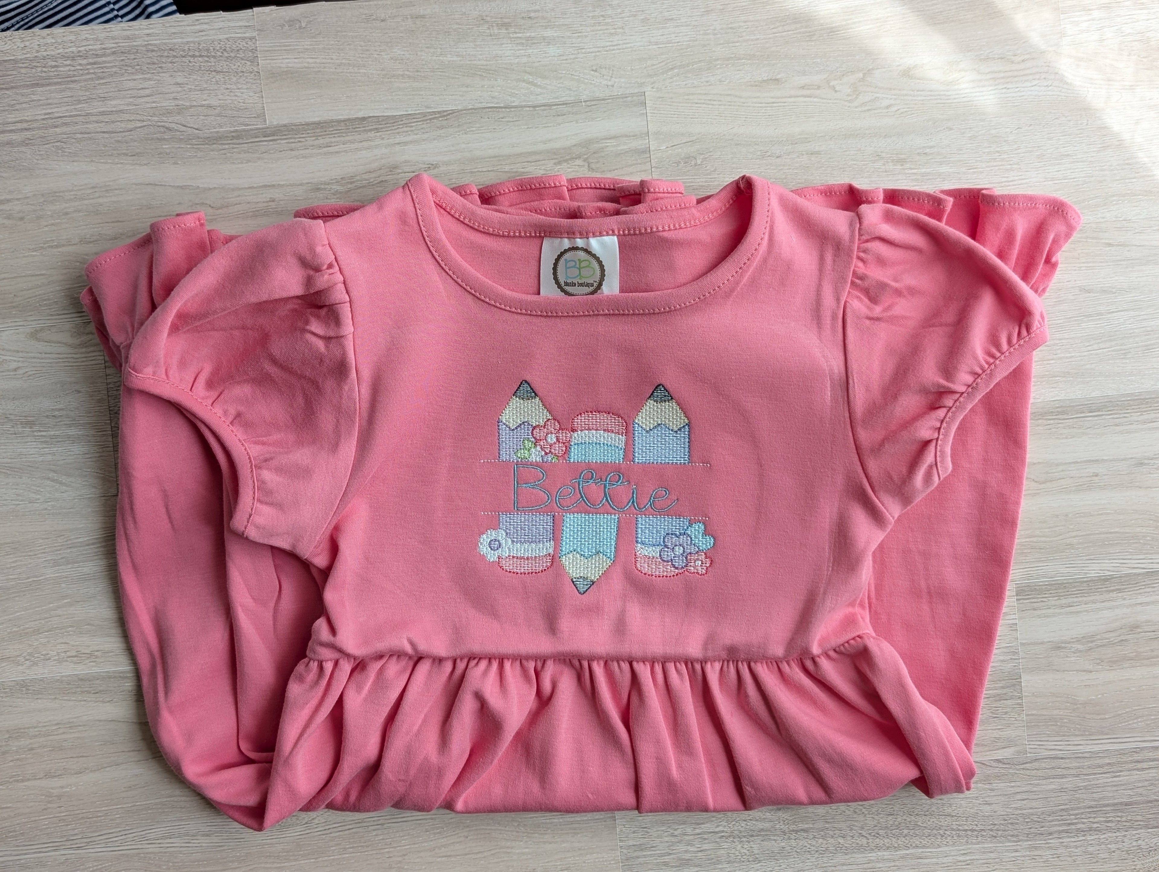 Pink flutter sleeve dress with floral pencil embroidery and personalized name, folded flat lay