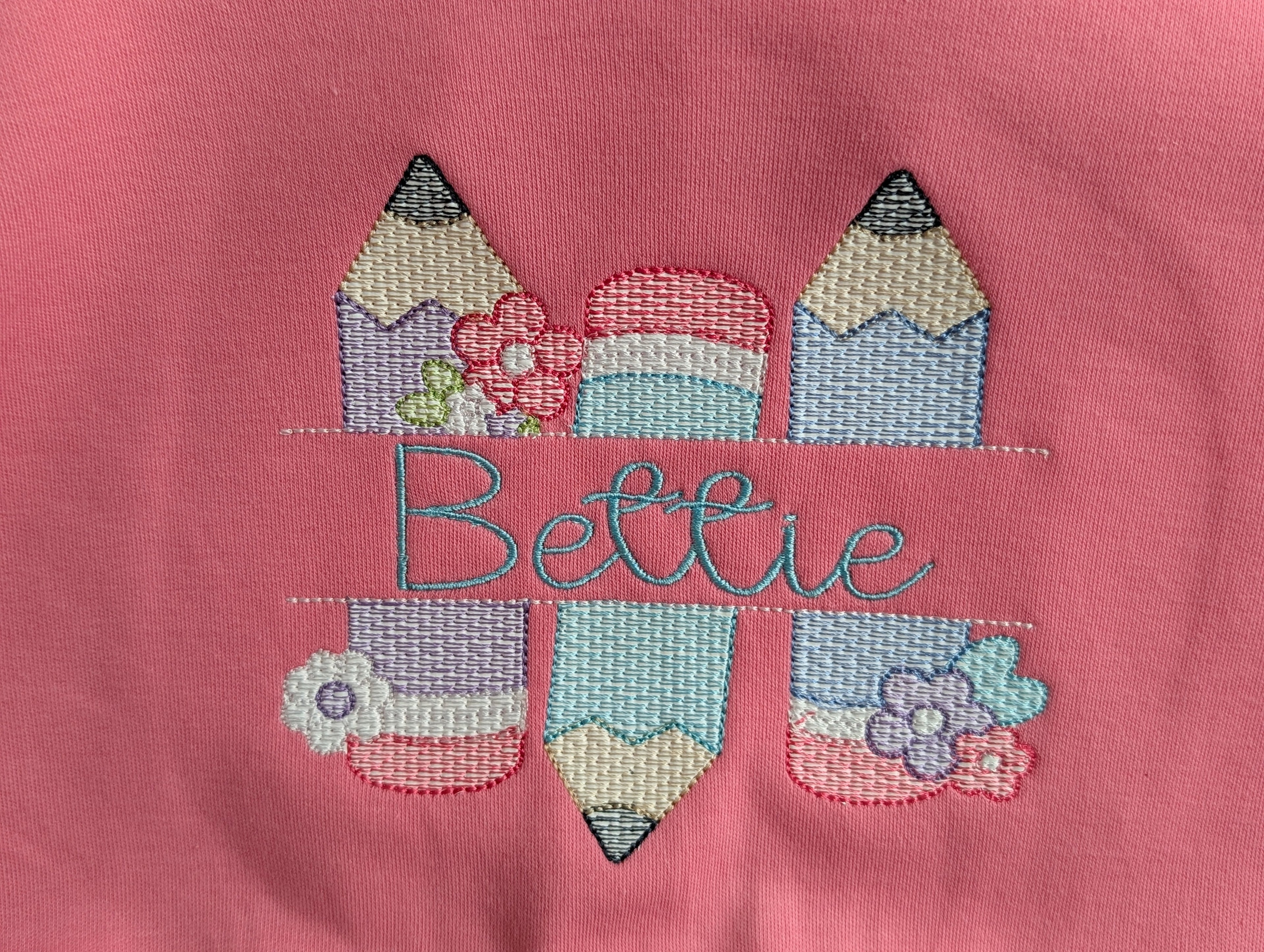 Close-up of floral pencil embroidery with custom script name in pastel colors