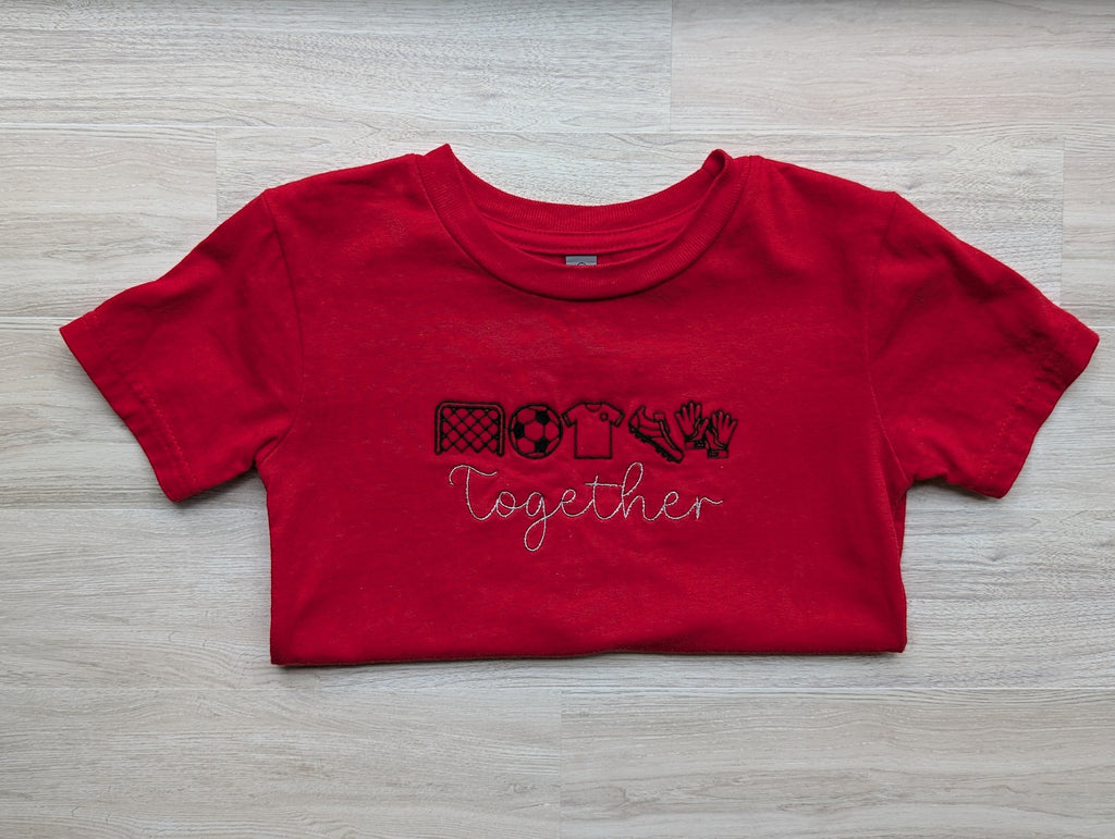 Red kids tee with Together soccer icons embroidery, folded flat lay
