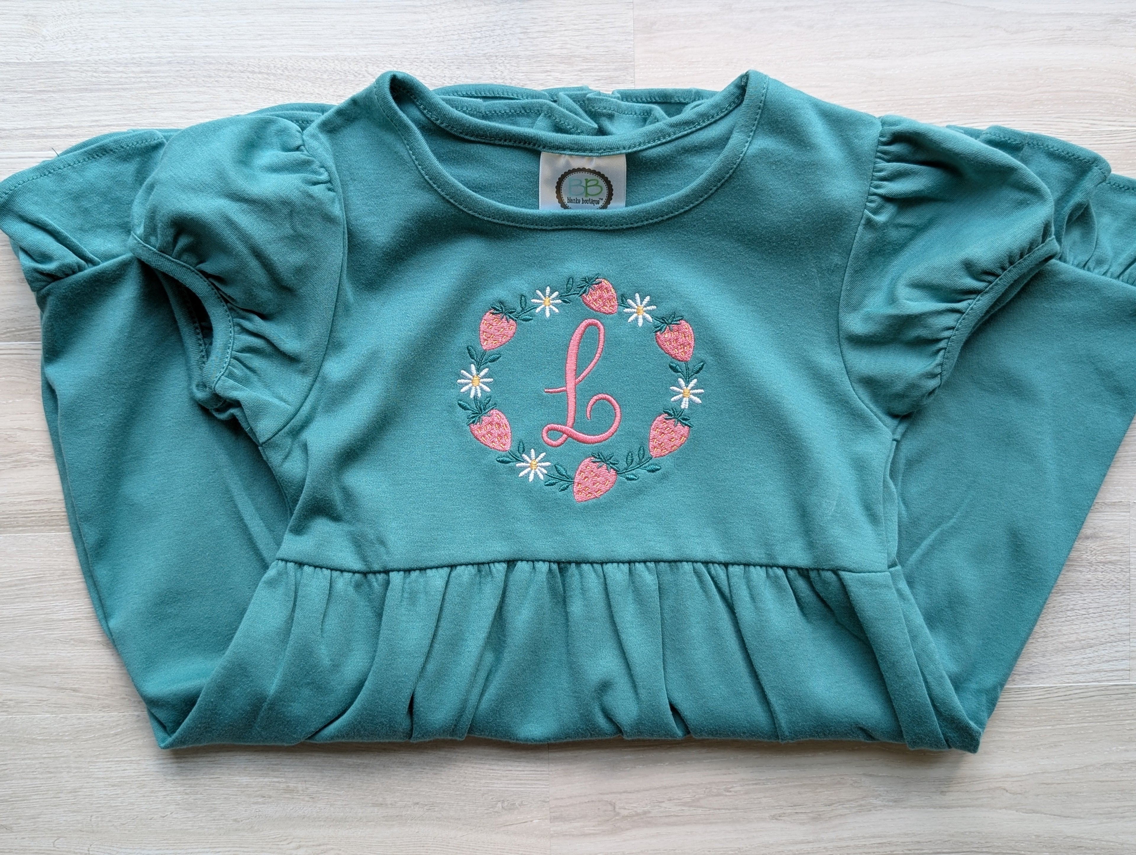 Teal embroidered girls dress with strawberry monogram wreath, hanging view