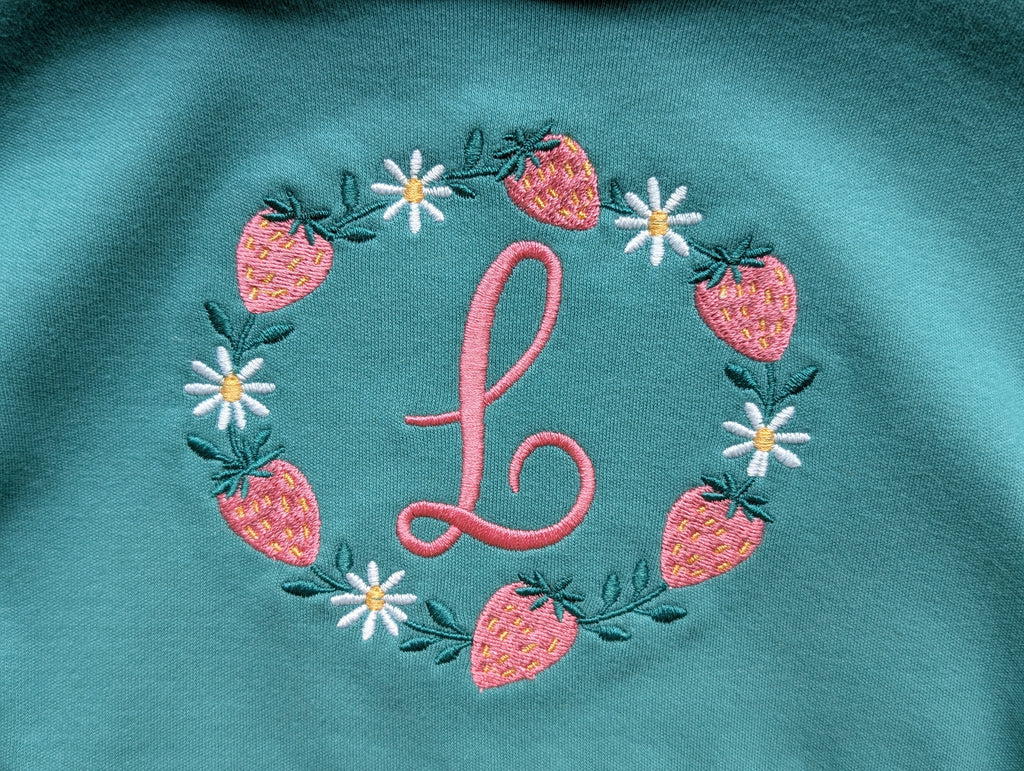 Close-up of strawberry and daisy embroidered monogram wreath