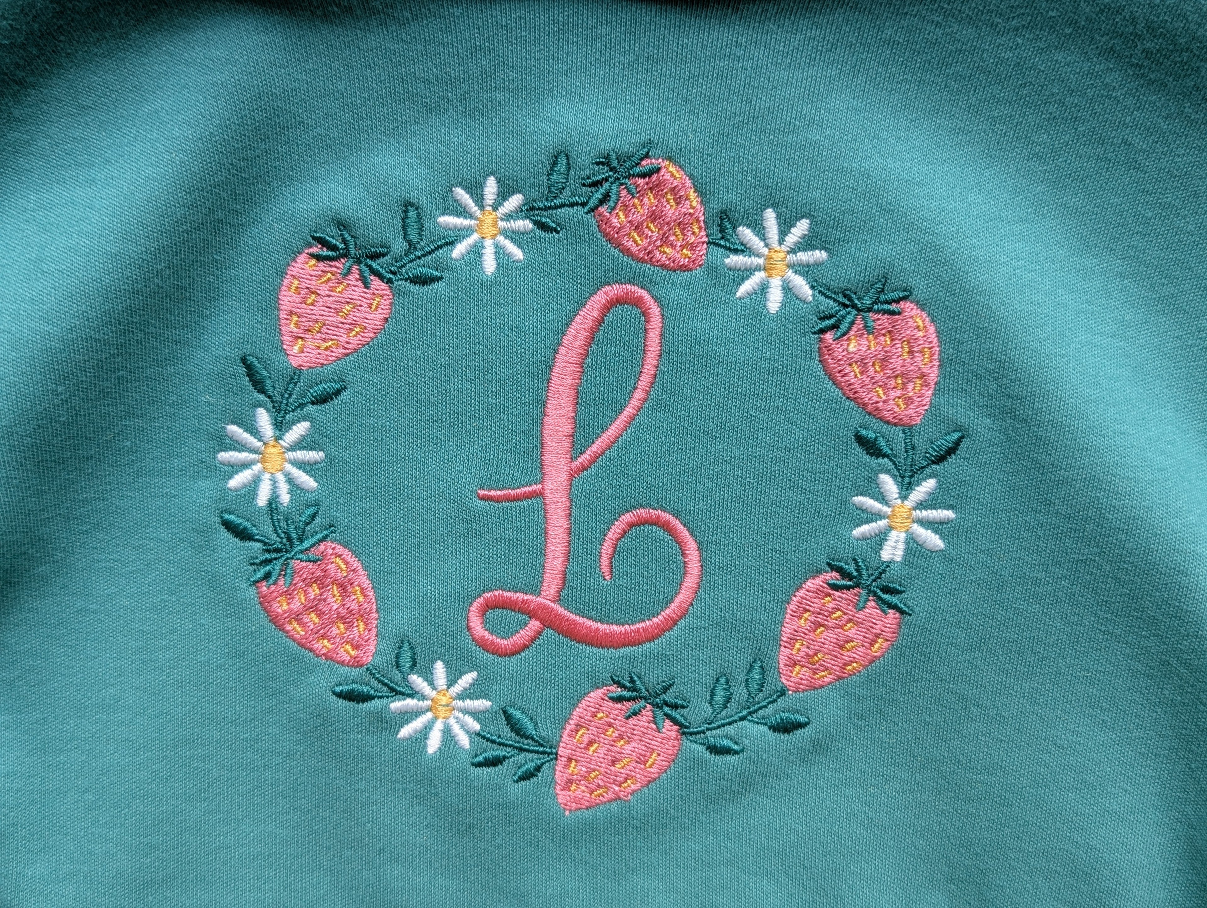 Close-up of strawberry and daisy embroidered monogram wreath