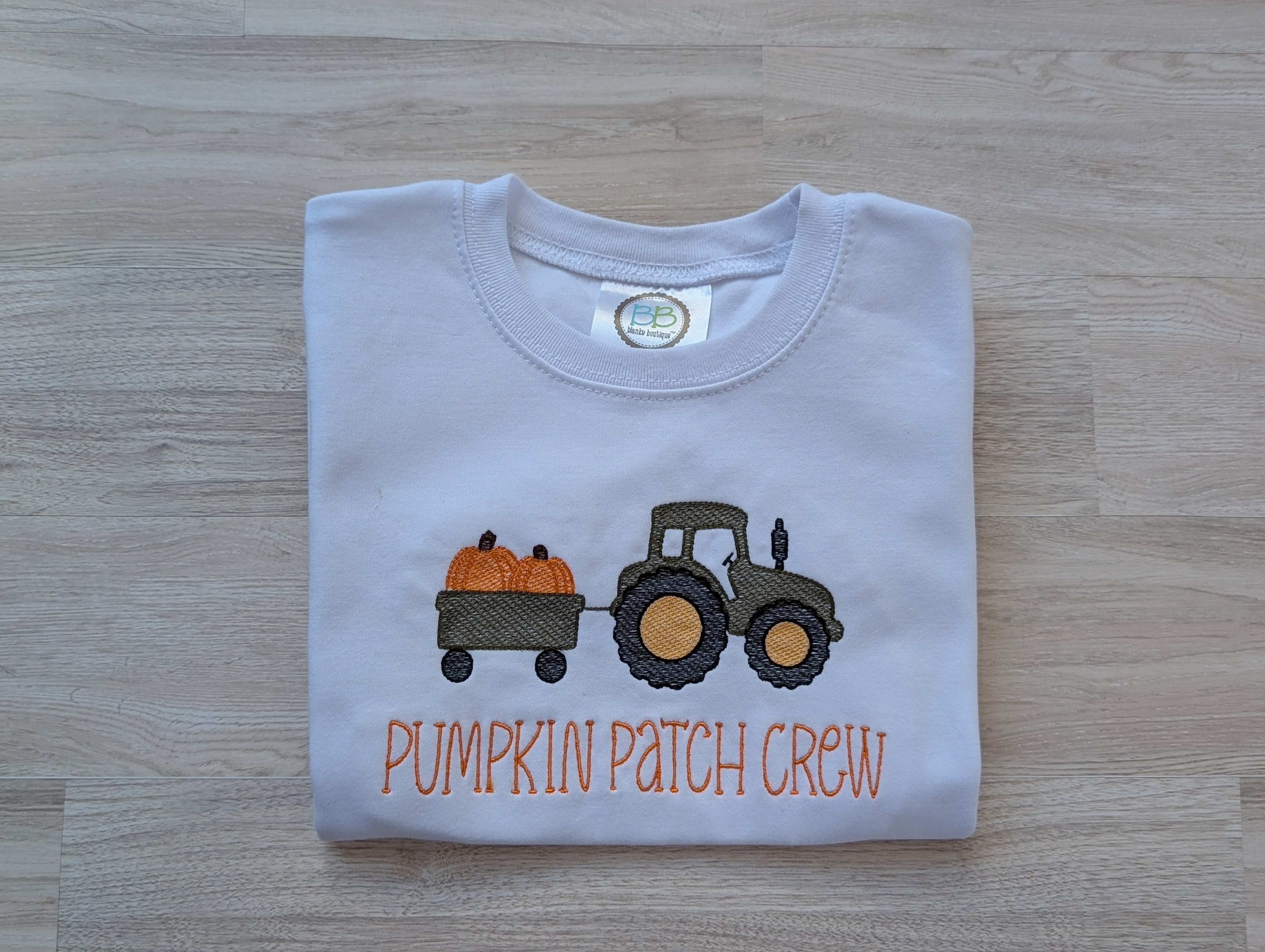 White kids tee with embroidered tractor hauling pumpkins and Pumpkin Patch Crew text, folded flat