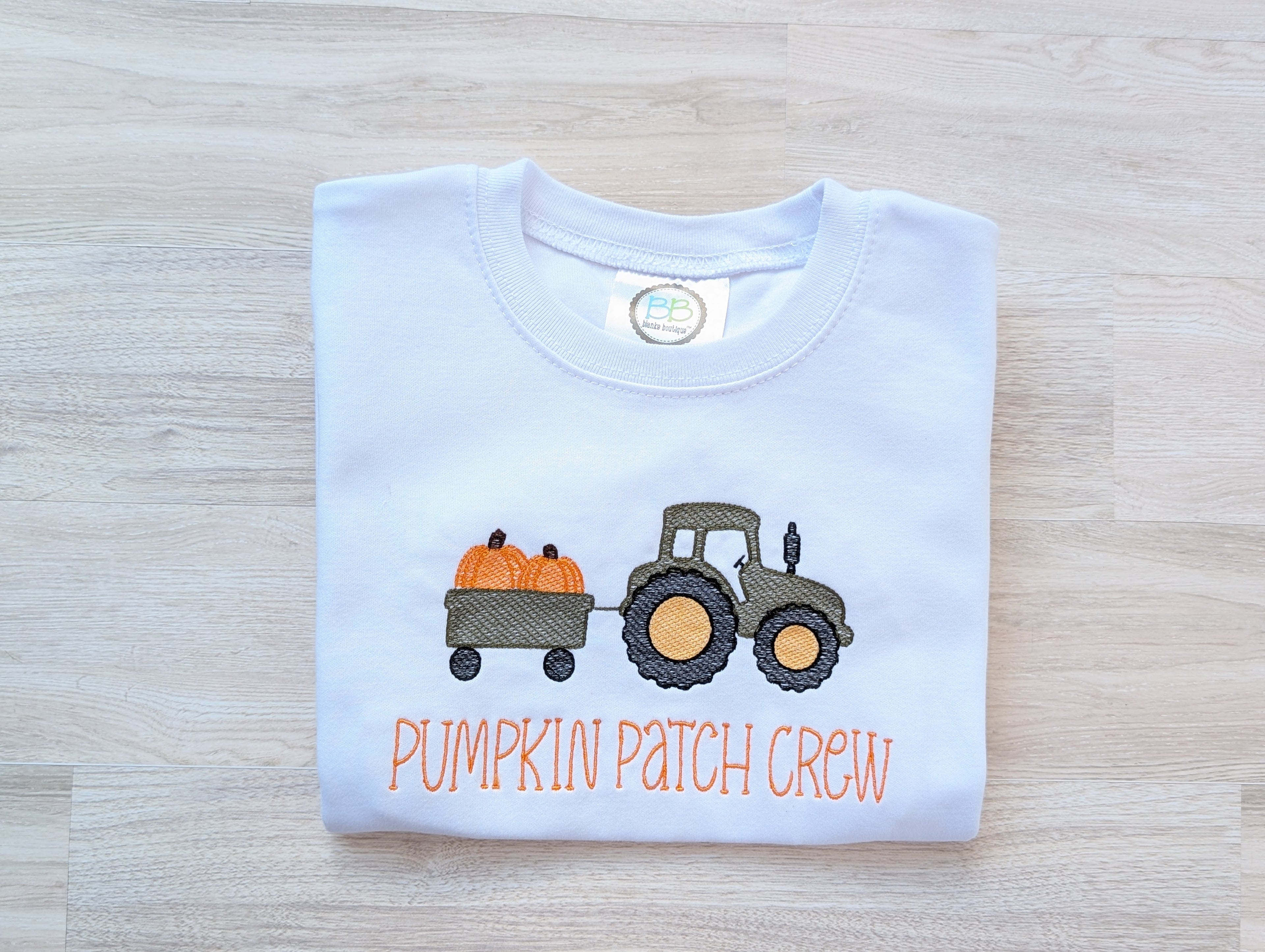 Side view of white kids tee showing Pumpkin Patch Crew embroidery and tractor detail