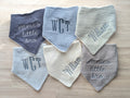 Six personalized baby bibs in assorted neutral shades with monograms, names, and short phrases