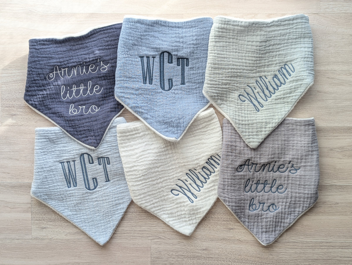 Six personalized baby bibs in assorted neutral shades with monograms, names, and short phrases