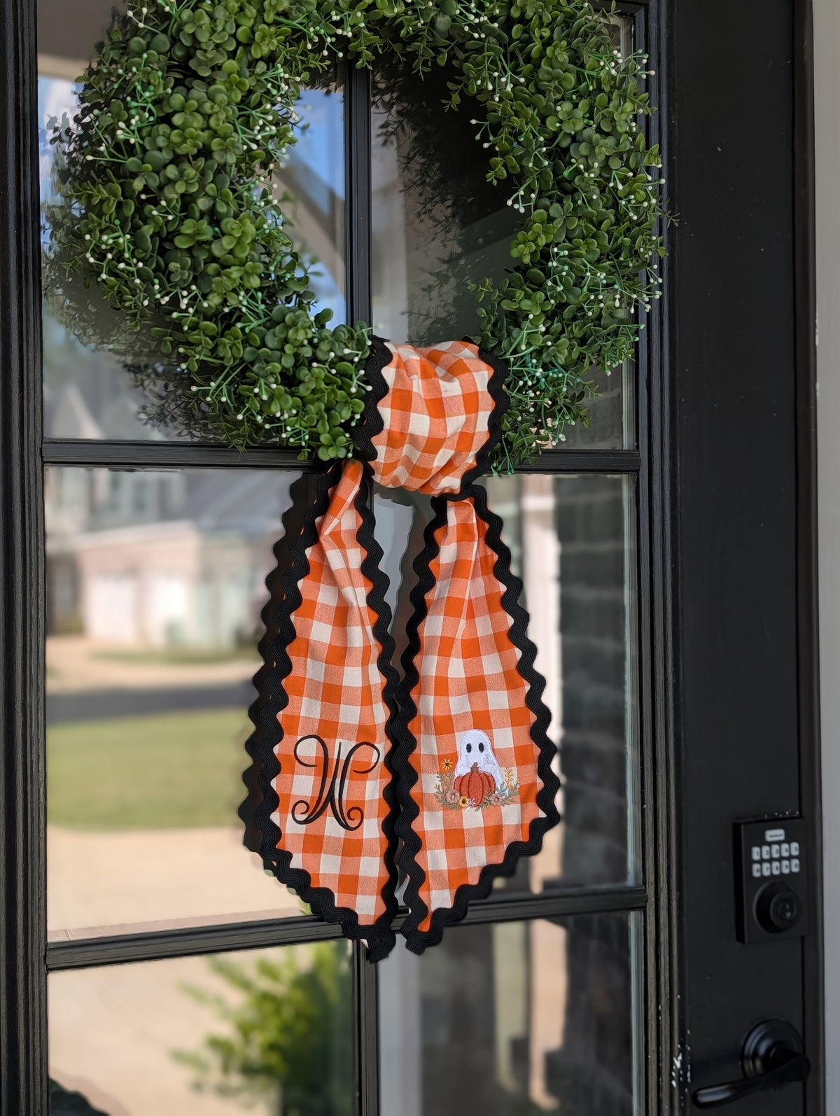 Ghost and pumpkin orange gingham wreath sash hanging on a front door wreath