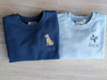 Close-up of airplane embroidery and Jack name on light blue sweatshirt